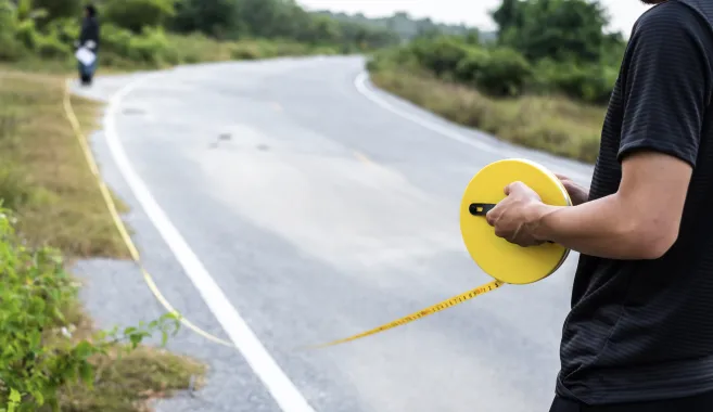Two people using a measuring wheel on the side of a road