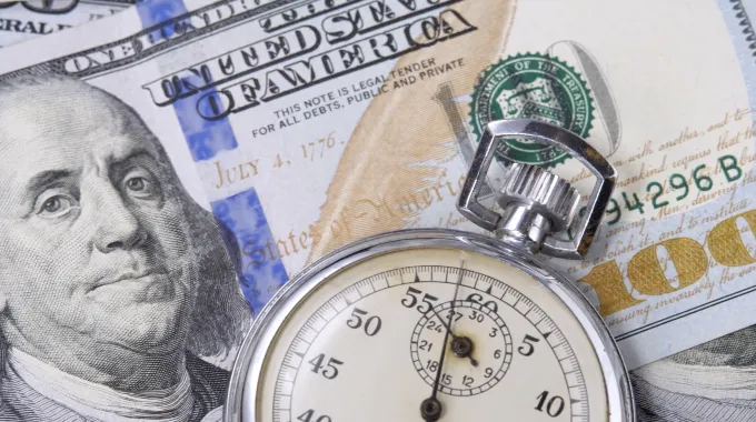 A time piece on top of a stack of one hundred dollar bills.
