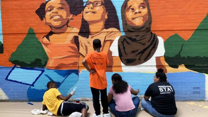 teenagers painting a mural on an outdoor building wall