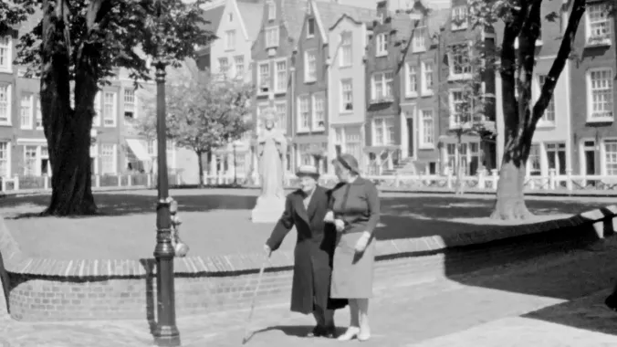 still from the movie of two people walking on  sidewalk with trees and buildings in the background