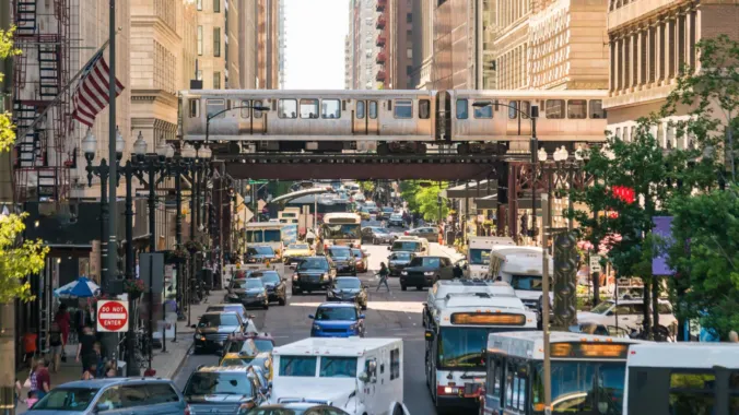 cars and buses on busy street with metro train in background