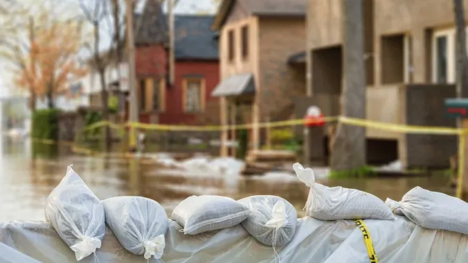 sandbags aligned horizontally with a flooded street and houses in the background