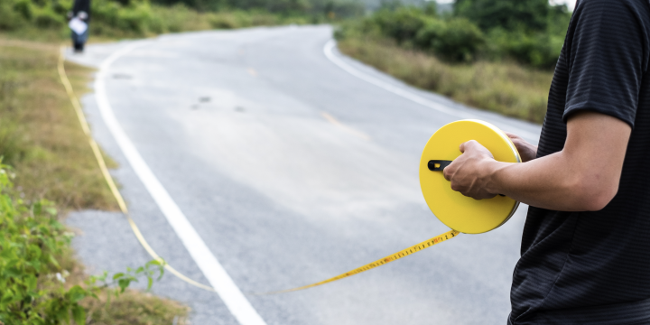 Two people using a measuring wheel on the side of a road