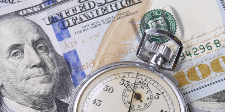 A time piece on top of a stack of one hundred dollar bills.