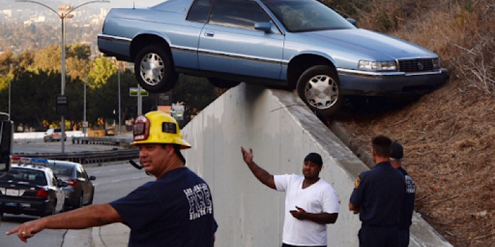 Car crashed into interstate wall with firefighters and people pointing.