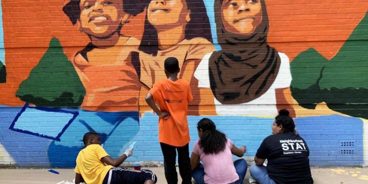 teenagers painting a mural on an outdoor building wall