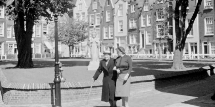 still from the movie of two people walking on  sidewalk with trees and buildings in the background