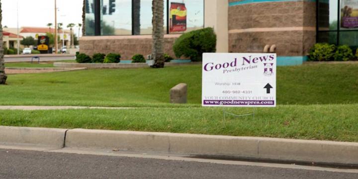 sign placed in grass next to street