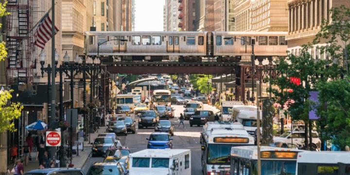 cars and buses on busy street with metro train in background