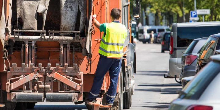 sanitation worker on the back of a garbage truck