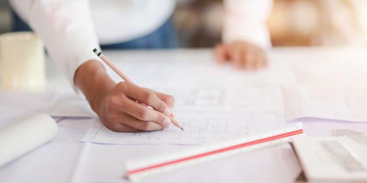 closeup of a hand holding a pencil and architectural drawings on a desk